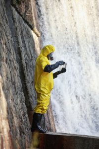 Scientist standing near waterfalls and wearing protective clothing.