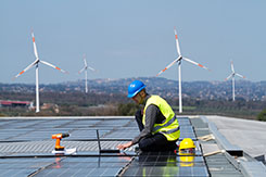 Worker installing solar panels with wind turbines in backdrop