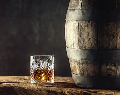 Liquor in a drinking glass, next to a barrel.