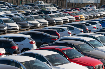 Outdoor parking lot of various types and colors of passenger vehicles in several rows.