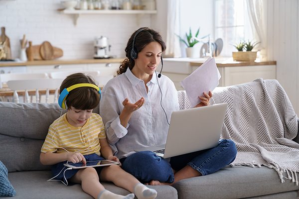 Woman and child sitting together on a couch, both using laptops or tablets