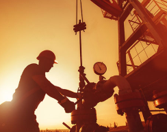 Silhouette image of worker and oil derrick.
