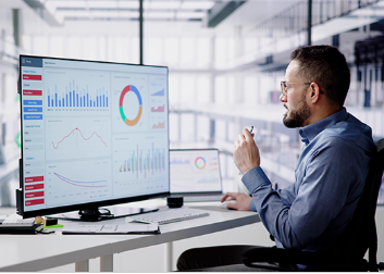 Man at work sitting at his desk in front of a computer with charts and graphs on the screen.