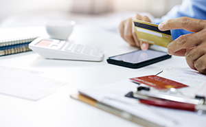 Male hand holding a bank card while using a calculator