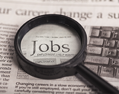 Magnifying glass looking at a newspaper closely with the word Jobs underneath it.