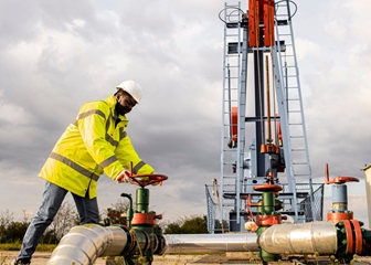 Male oil and gas worker closing an industrial valve by an oil rig
