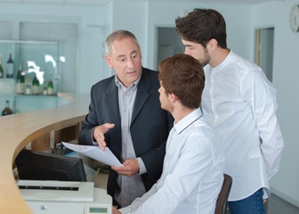 Three men in training, looking at a computer behind the reception desk.