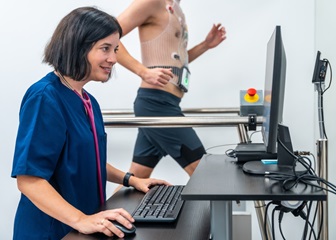 A cardiovascular technician looking at a computer screen while a patient walks on a treadmill during a stress test
