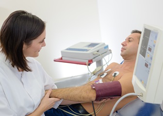 A cardiovascular technician taking the blood pressure of a patient with electrodes attached to his chest