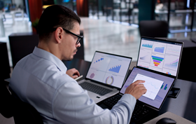 Male analyst using multiple laptops to analyze financial data.
