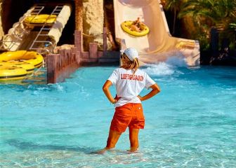 A female lifeguard standing in the water at the base of a waterslide.