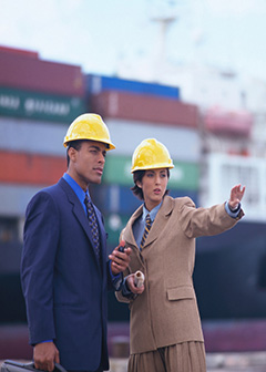 Male and female logisticians outside talking with hardhats on.