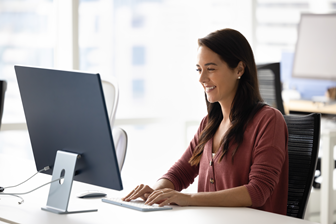 Worker sits at desk and works on desktop computer. 