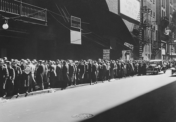 Men stand in a bread line in a black and white image from the Great Depression.