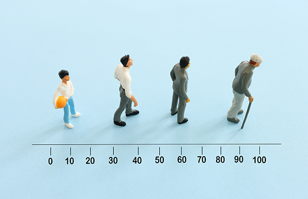 Four people in a row showing the progression from youth to old age.