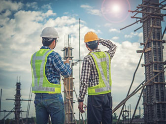 Two male civil engineers looking towards wooden structures with a tablet in hand.