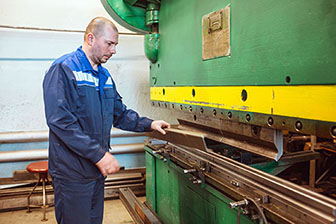 Male worker holding a piece of metal next to a metal press.