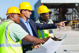 Industrial engineer and two coworkers looking at paper blueprint at a construction site.
