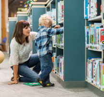 Woman kneeling mext to a child while reaching for an item on a low shelf
