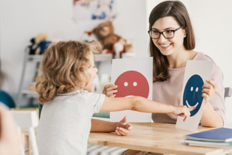 Child pointing at smiley face held by school psychologist.