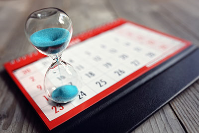 Hourglass with blue sand resting on a calendar.