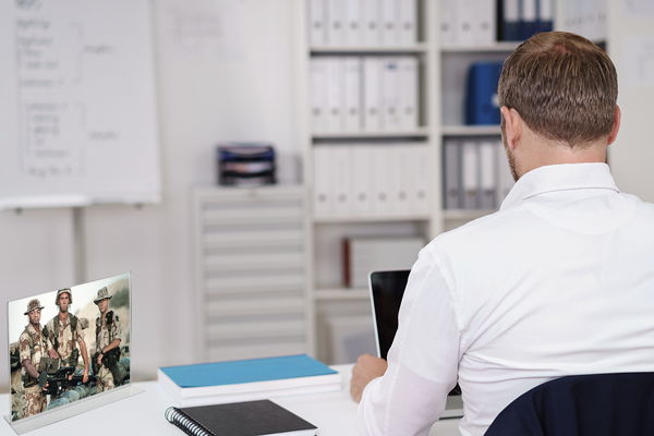 Civilian man working at a desk, with a picture of friends from military